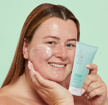 Joyful woman displaying Tribe Gentle Balm Cleanser product on her right face, holding the bottle in her left hand, featured on Spa Circle Brands' product listing.