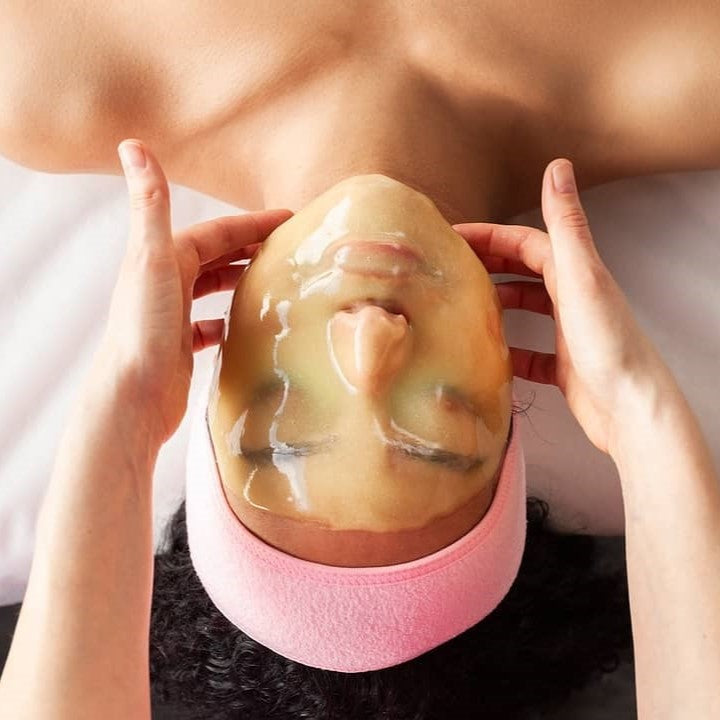 A woman getting a facial treatment with Brightening Complex Hydrojelly Mask, featured on Spa Circle Brands page.